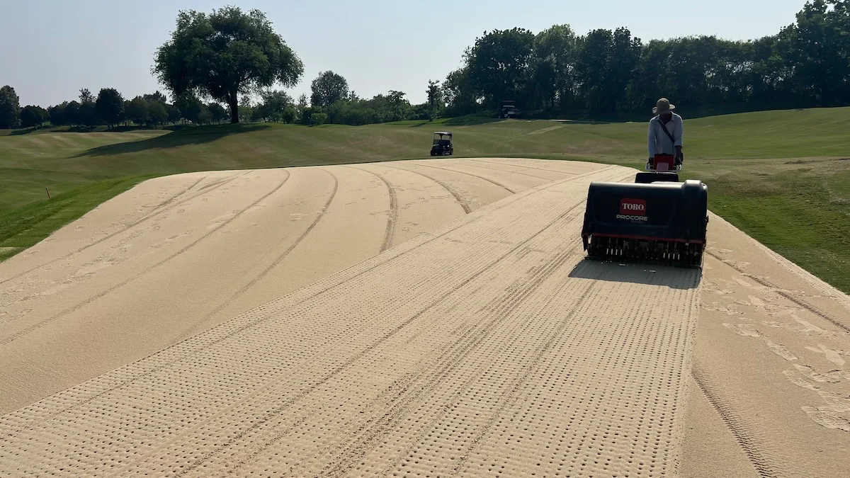 Aerating a golf putting green after topdressing